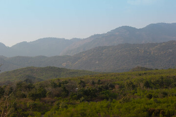 Fototapeta premium Aerial top view above green pass to rocky deep gorge with sharp sheer crags silhouettes in blue sky. Dramatic layered scenery