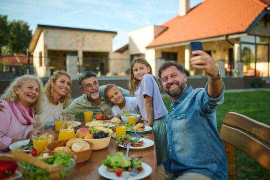 Happy family taking a selfie while having lunch in the backyard - Powered by Adobe