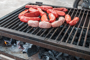 Barbecue scene showing chorizo sausages being grilled over hot coals with flames rising below