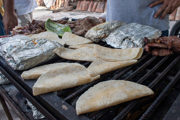 Delicious quesadillas cooking on a grill alongside foil-wrapped food and meat. Authentic Mexican...