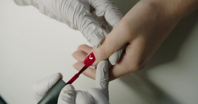 Nail care treatments. Manicurist paints client nails with bright red polish. Manicure master hands in gloves applying red gel polish on client nail at beauty salon. Professional care for female hands.