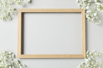 Top view photo with gypsophila flowers and wooden frame on gray background 