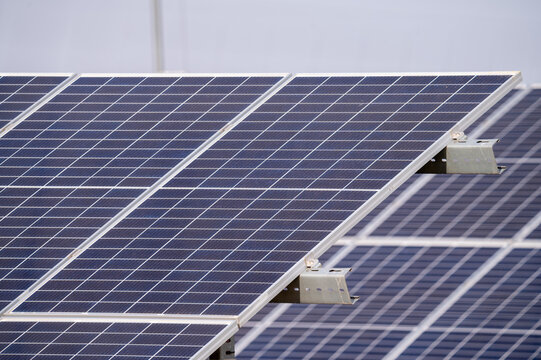 A detailed close-up view of solar panels installed in a photovoltaic power plant. The blue solar cells are aligned in a structured array, capturing sunlight for renewable energy generation. The metall