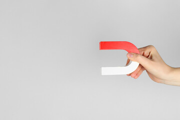 Woman with horseshoe magnet on grey background, closeup. Space for text
