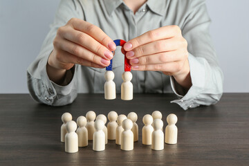 Woman with magnet attracting human figures at wooden table, closeup