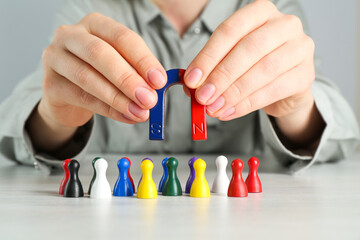 Woman with magnet attracting colorful game pieces at light table, closeup