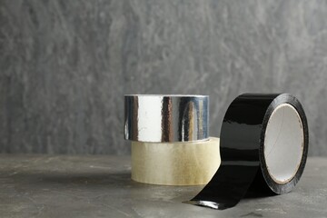 Rolls of different adhesive tapes on grey table, space for text