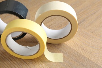 Rolls of different adhesive tapes on wooden table, closeup