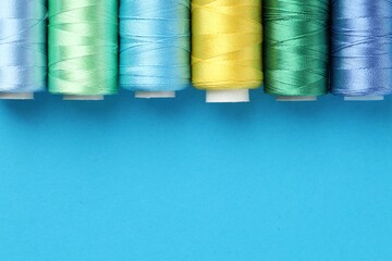Different spools of sewing threads on light blue background, flat lay. Space for text