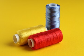 Different spools of sewing threads on yellow background, closeup