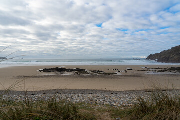 Vue sur la plage de la baie des Trépassés à marée basse, bordée de falaises. La Pointe du Raz se profile au loin sous un ciel voilé, les vagues créant une légère écume sur le sable.
