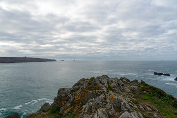 Naklejka premium Vue panoramique sur la Pointe du Raz et la baie des Trépassés depuis les falaises, avec un ciel cotonneux qui enveloppe le paysage.