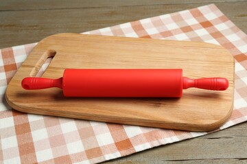 Red rolling pin and board on wooden table, closeup