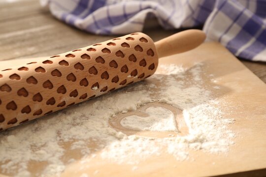 Rolling pin and heart shape made of flour on table, closeup