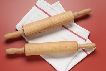 Wooden rolling pins and napkin on red background, flat lay