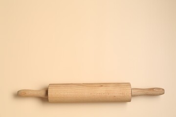Wooden rolling pin on beige background, top view. Space for text