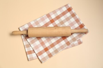 Wooden rolling pin and checkered napkin on beige background, top view