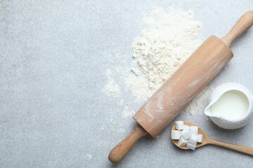 Rolling pin, flour, sugar cubes and milk on light grey table, flat lay. Space for text