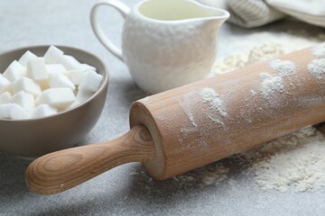 Rolling pin, flour, sugar cubes and milk on light grey table, closeup