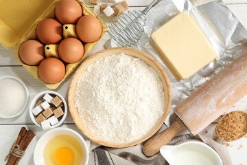 Rolling pin and ingredients for dough on white wooden table, flat lay
