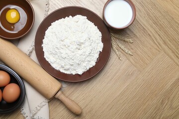 Rolling pin and ingredients for dough on wooden table, flat lay. Space for text