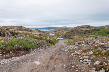 Winding gravel road on the Sredniy Peninsula, Murmansk region, Russia. Bay of the Barents Sea in the distance