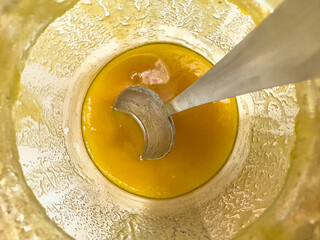 Inside an almost empty honey jar, golden contents and a spoon are visible.