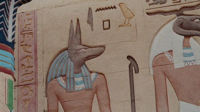 Ancient Egyptian wall relief depicting Anubis, god of the dead. The intricate artwork showcases vibrant colors and detailed hieroglyphics, rich history and mythology of ancient Egypt.