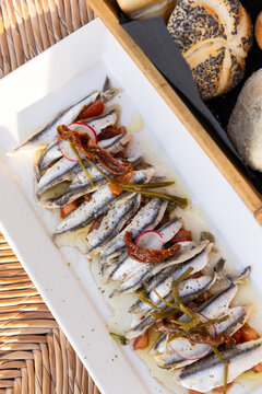 Marinated anchovies with olive oil, peppers, and radish on a white rectangle plate served at a restaurant in Paros, Greece.