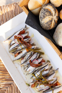 Marinated anchovies with olive oil, peppers, and radish on a white rectangle plate served at a restaurant in Paros, Greece.