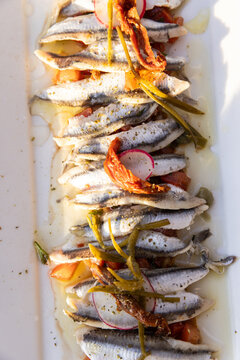 Marinated anchovies with olive oil, peppers, and radish on a white rectangle plate served at a restaurant in Paros, Greece.