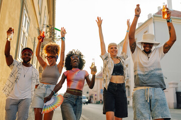 Young people having fun walking down the street drinking and raising their arms