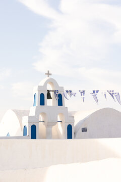 Blue and white traditional church on Santorini, Greece, with Greek flags hanging in the breeze on a clear day.