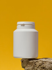 White plastic medicine jar on stone, yellow background. Mock up