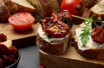 Ciabatta spread with cream cheese, topped with wedges of dried tomatoes with spices on the table, appetizer
