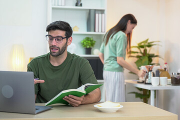 Fototapeta premium Young professional freelancing at home, texting on a phone in a stylish, well-lit living room. A woman enjoying on the sofa in the background