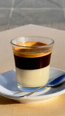 Close-up of a café bombón served in a glass cup with layers of condensed milk and espresso on a terrace table