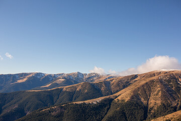 Naklejka premium hills and mountain peaks covered in fog and light snow, before spring, under a bright sun and a clear blue sky