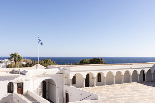 Architectural image of a whitewashed church in Greece with views of the ocean and sky in the background on a sunny day. 