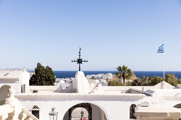 Architectural image of a whitewashed church in Greece with views of the ocean and sky in the background on a sunny day. 