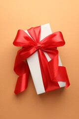 Gift box with red bow on coral background, top view