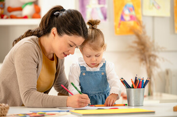A caring teacher interacts with a shy young girl in a classroom, encouraging her to engage in a...