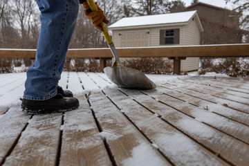 Close up view of an unidentifiable person shoveling light snow off a wooden deck on an overcast...