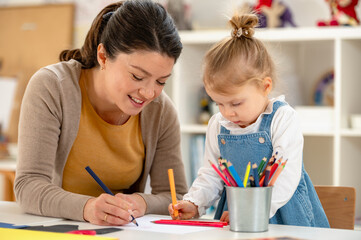 A caring teacher interacts with a shy young girl in a classroom, encouraging her to engage in a...