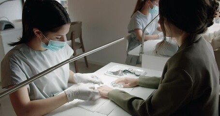 A manicurist treats a woman's cuticles using a manicure machine in a nail salon under the supervision of a teacher who processes a nail with nail scissors. Nail extension.