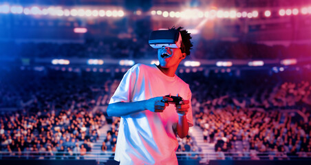 Fototapeta premium Adult holding joystick and wearing VR goggles while enjoy playing games at stadium with blurring background. African man enjoy controlling controller and using augmented reality technology. Ingenuity.