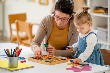 A caring teacher and a toddler girl play with wooden letters, exploring language and early literacy...