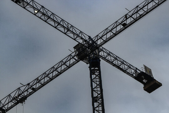 Crossing construction cranes under a cloudy sky