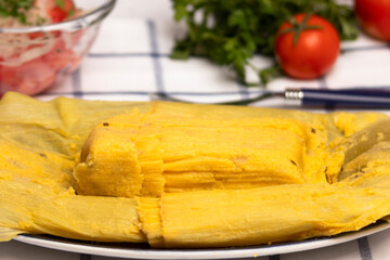 detalle en primer plano de una humita en hojas, comida típica chilena, al fondo tomates maduros y hierbas