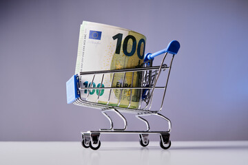 A shopping cart is filled with 100 euros. The cart is on a table. Concept of shopping and the value...